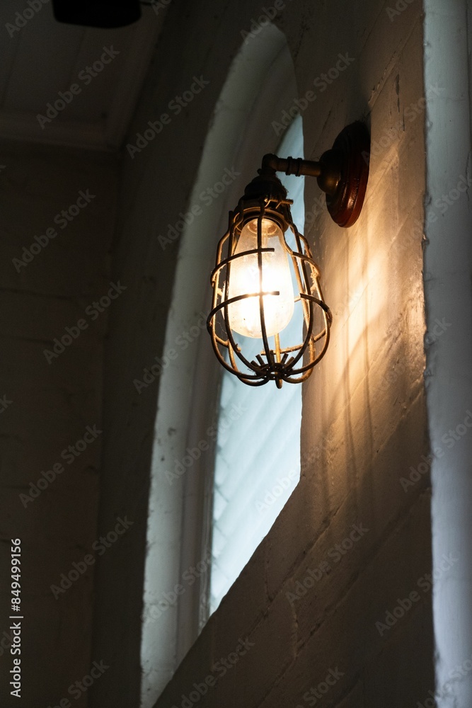Obraz na plátně Vintage wall-mounted light fixture illuminating a brick wall next to an arched w