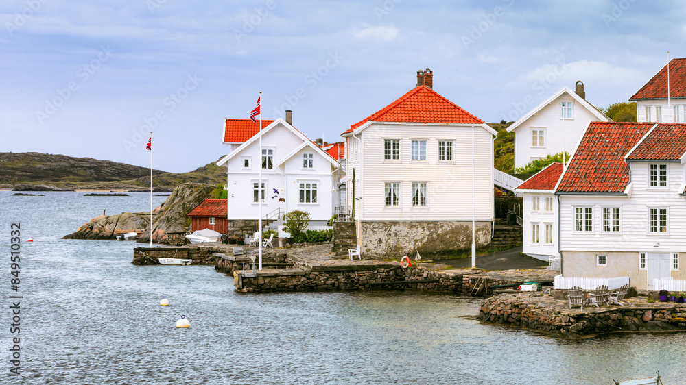 Fototapeta premium Traditional white wooden houses with red-tiled roofs by waterfront in beautiful fishing village. Cold destinations travel trend. Farsund, Norway