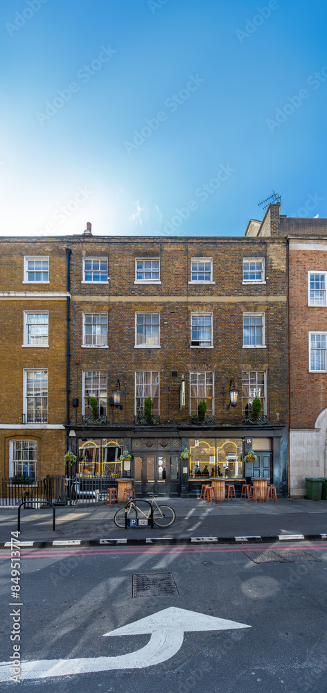 Fototapeta premium Typical facade of an English brick building with the typical London pub, a parked bike and a traffic sign painted on the asphalt indicating a turn under a clear blue sky. London.
