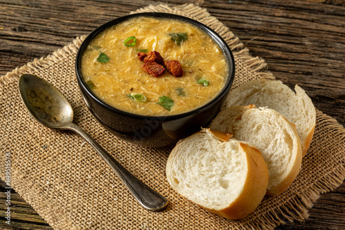 Caldo de Kenga Cassava broth with shredded chicken, typical Brazilian food known as (Caldo de Quenga), in a black pot on top of a rustica with a spoon and slices of bread,  with selective focus photo