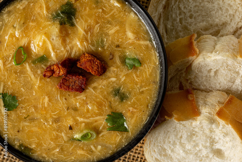 Caldo de Kenga Cassava broth with shredded chicken, typical Brazilian food known as (Caldo de Quenga), in a black pot on top of a rustica with a spoon and slices of bread,  with selective focus photo