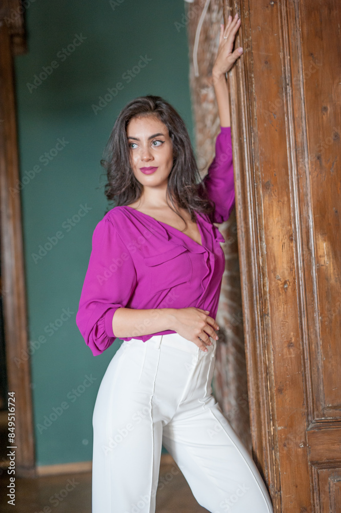 Beautiful young brunette woman in a purple blouse and white pants posing outdoor. Portrait of a beautiful young brunette woman with long hair posing fashion