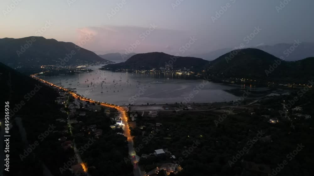 An aerial view of Lefkadas harbor at night, capturing the citys twinkling lights reflecting on the calm waters, surrounded by lush, dark mountains. An aerial view of Lefkadas harbor at night, capturing the citys twinkling lights reflecting on the calm waters, surrounded by lush, dark mountains.