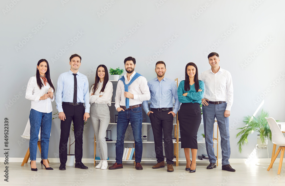 Obraz premium Full length portrait of business people men and women looking at camera and smiling indoors. Company employees team or group of staff standing in office confidently. Business people portrait.