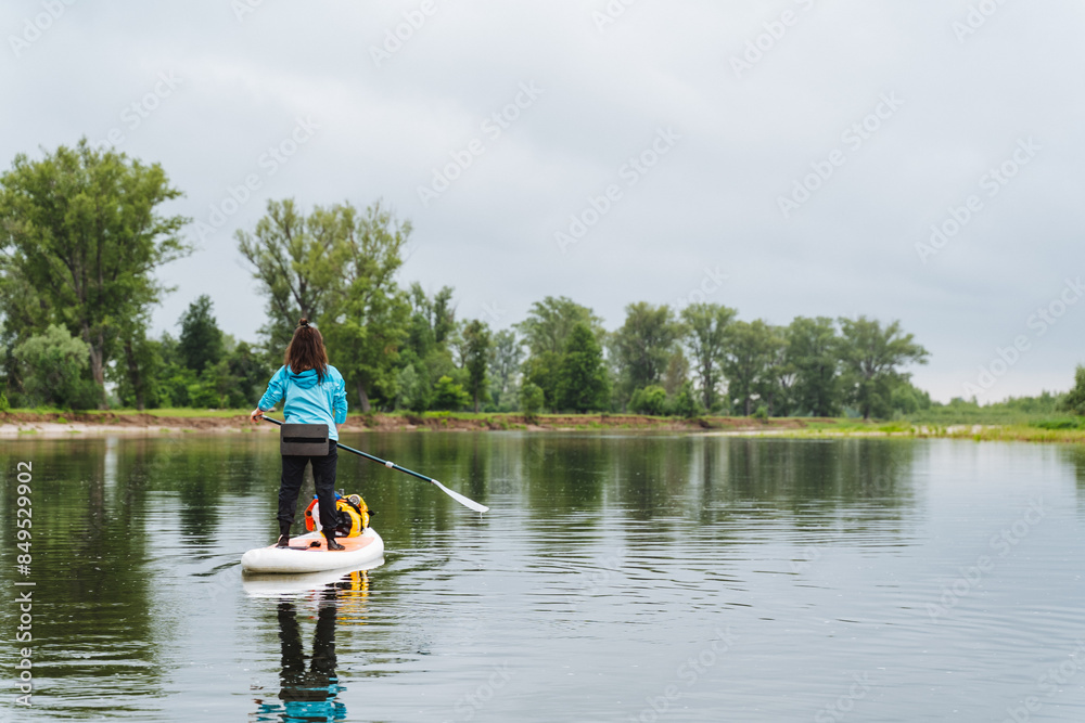 Enjoy the tranquil outdoor adventure of a woman paddleboarding on a serene lake with her dog, surrounded by greenery. Its a peaceful and calming experience in nature