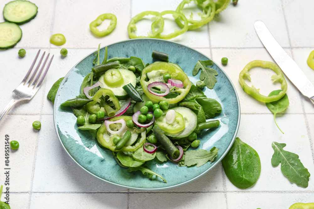 Plate of fresh vegetable salad and ingredients on white tile background Plate of fresh vegetable salad and ingredients on white tile background