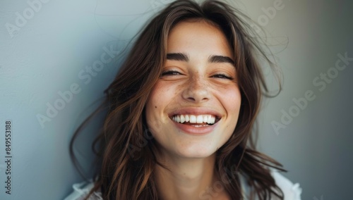 A beautiful woman smiles with perfect teeth and radiant skin, radiating confidence against a grey background. A portrait of a laughing young model shows a healthy white smile after dental treatment
