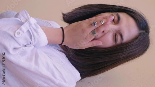 Vertical video of a 22-year-old woman with a gray tank top and white blouse, yawning widely. The shot captures her tired and sleepy expression.