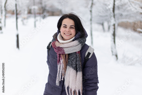 Young smiling beautiful woman wearing scarf outdoors during snowfall