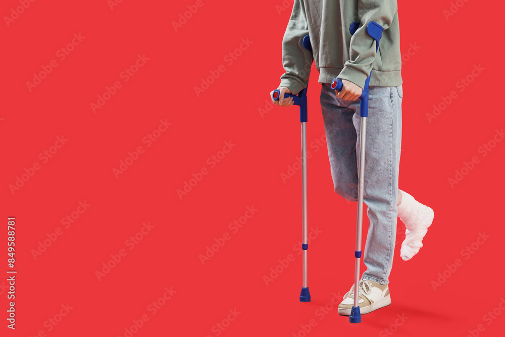 Injured young woman after accident with broken foot and crutches on red background Injured young woman after accident with broken foot and crutches on red background