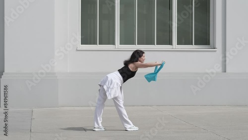 A woman performs a strength training routine with fitness bands in an urban setting. The minimalistic background emphasizes the practicality of integrating fitness into daily city life. photo