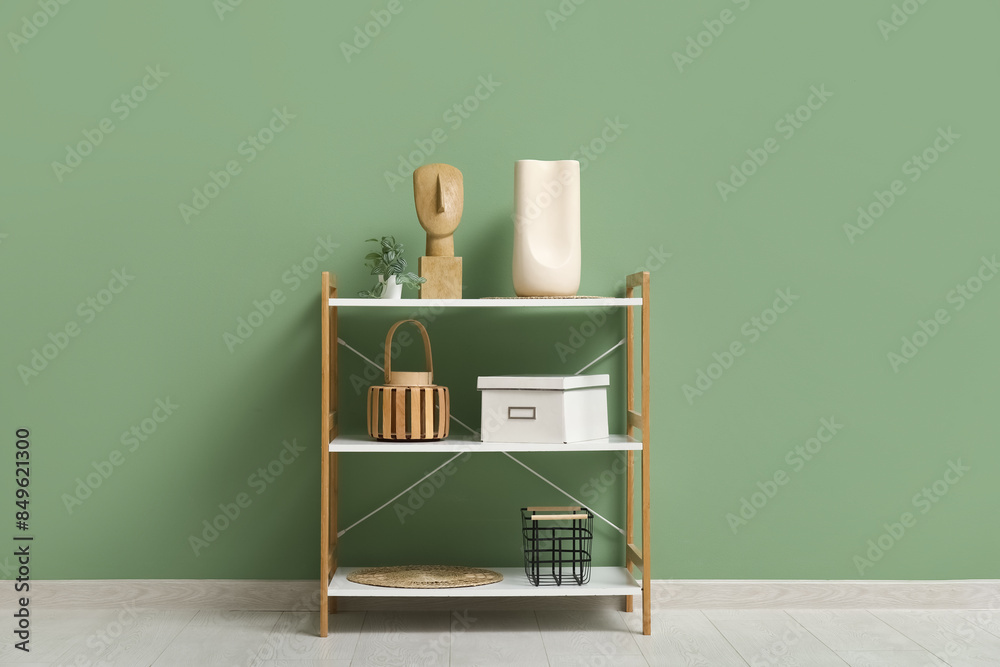 © Pixel-Shot - Modern shelving unit with houseplant and decor near green wall