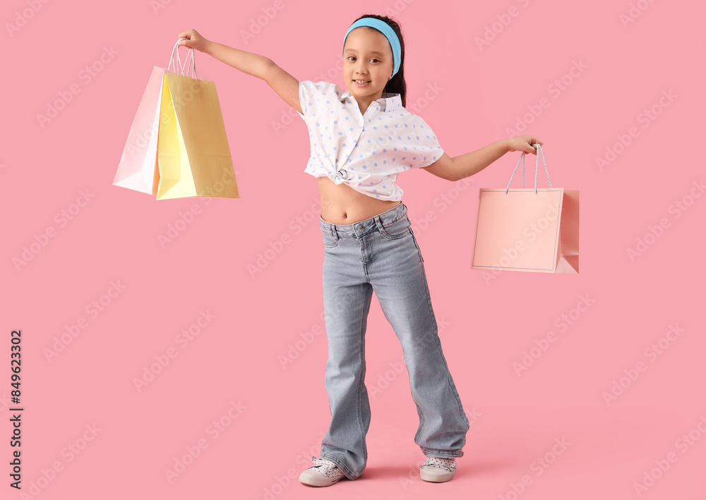 Fototapeta premium Portrait of fashionable little girl with shopping bags on pink background