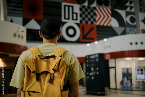 Young man at the airport looking at the list of destinations, rear view. Tourist guy with yellow backpack waits for a train at a train station. A new railway station in Belgrade, Serbia. photo