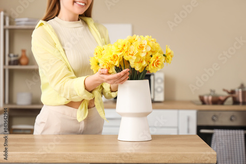 Woman touching daffodil flowers in vase in kitchen