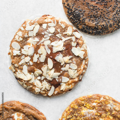 Overhead view of different types of sugar cookies, almond chocolate chip cookies, cornflake white chocolate chip cookie, black sesame sugar cookie on parchment paper photo