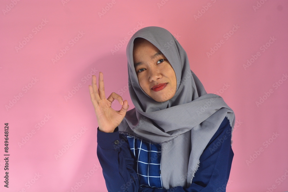 Cheerful and enthusiastic young Asian woman in hijab looks at the camera and shows the OK hand gesture Cheerful and enthusiastic young Asian woman in hijab looks at the camera and shows the OK hand gesture