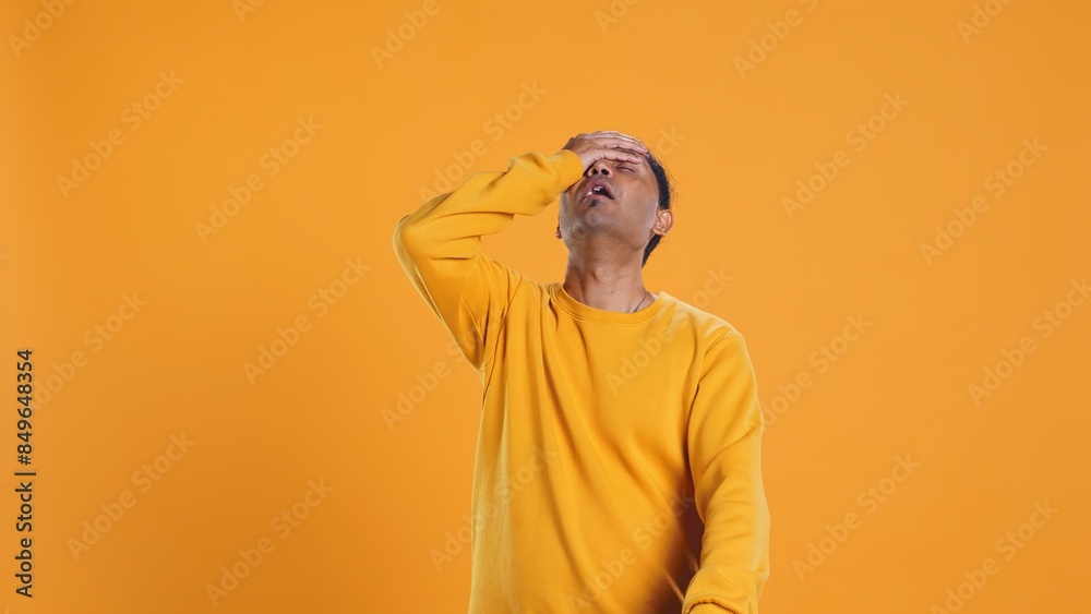 Fototapeta premium Delivery man doing face palm after realizing he forgot to put orders in thermal backpack. Upset courier making mistake, failing to remember to put lunch boxes in bag, studio background, camera B