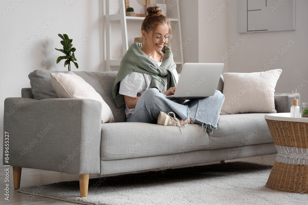 Young woman in eyeglasses sitting on sofa and chatting with laptop in living room Young woman in eyeglasses sitting on sofa and chatting with laptop in living room