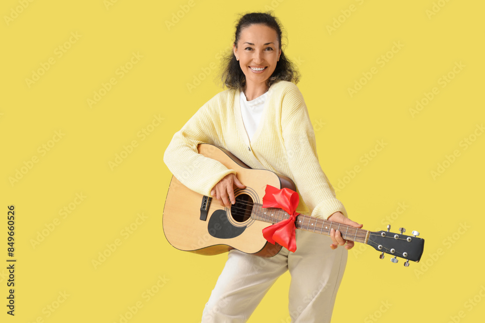 Fototapeta premium Mature woman with gift guitar on yellow background