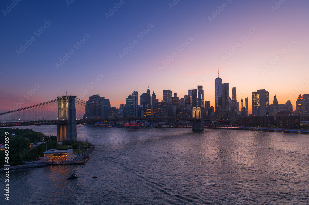 Fototapeta premium Brooklyn Bridge and New York skyline across the East River under an intense sunset.