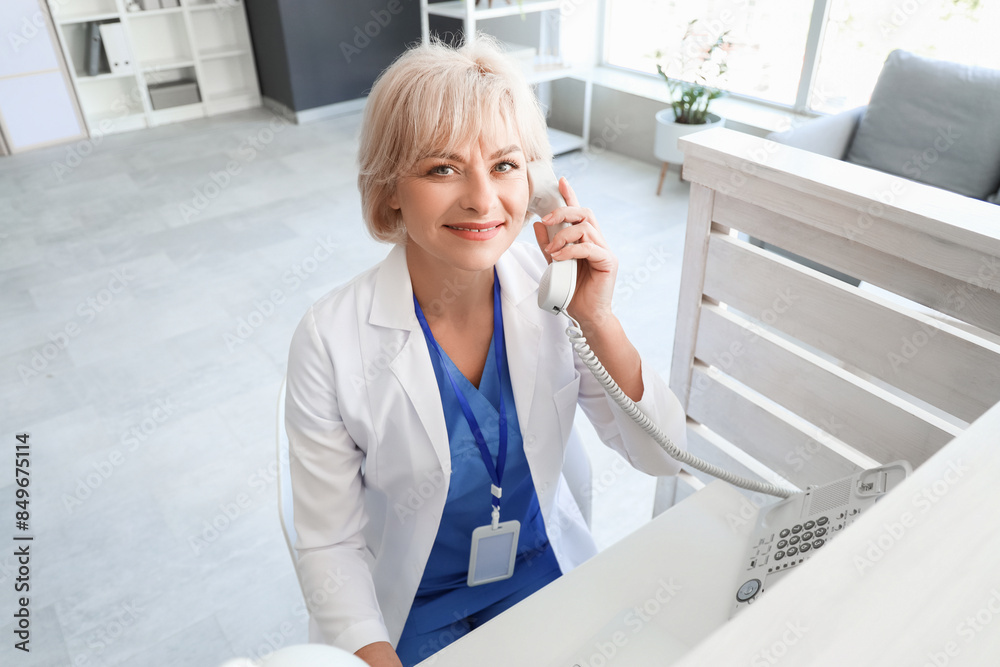 Female doctor talking by phone at reception desk in clinic Female doctor talking by phone at reception desk in clinic
