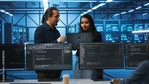 Programmer and supervisor in server room looking for equipment misconfigurations, doing brainstorming. Multiracial colleagues checking data center gear bottlenecks leading to glitches photo