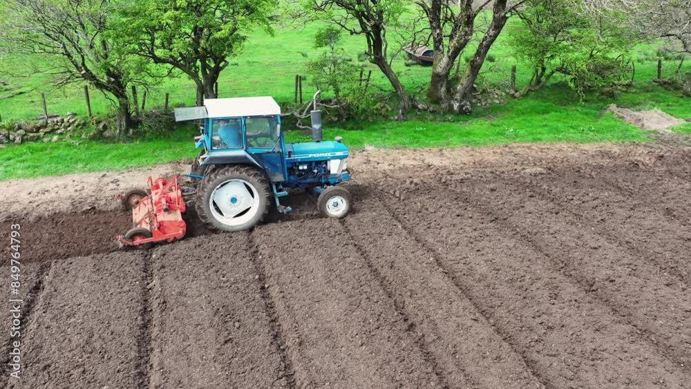 Aerial video of a blue tractor rotovating a field for crops at a farm Aerial video of a blue tractor rotovating a field for crops at a farm