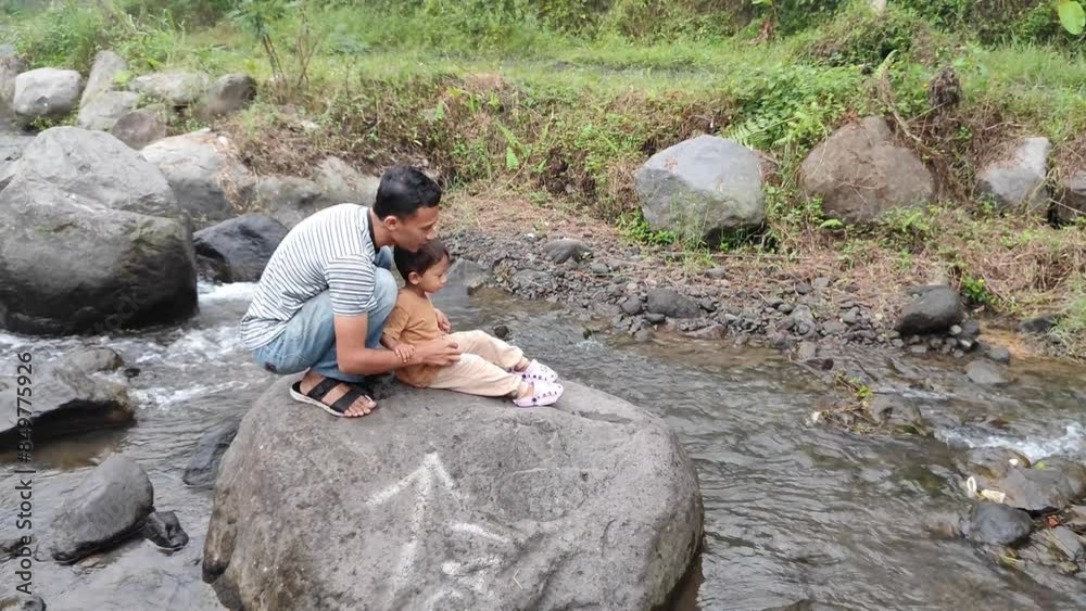 A young father was playing with his son on a large river rock A young father was playing with his son on a large river rock