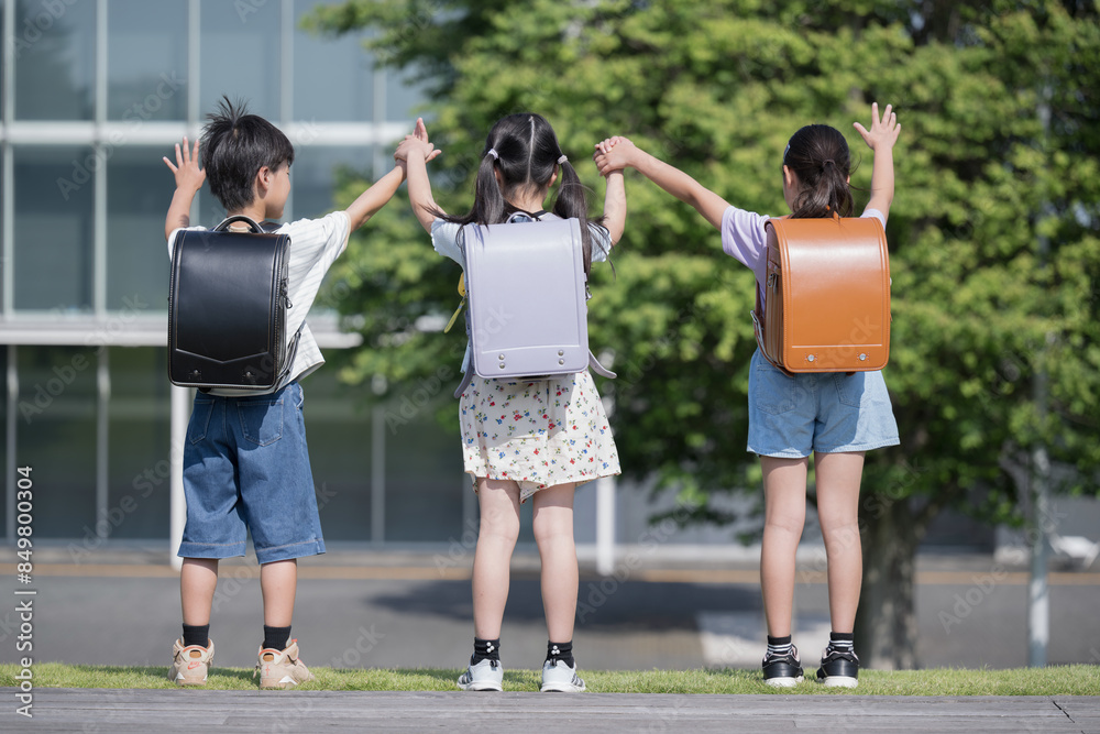 校舎の前でランドセルを背負った小学生たちの後ろ姿顔無し 手を挙げるバンザイ 校舎の前でランドセルを背負った小学生たちの後ろ姿顔無し 手を挙げるバンザイ
