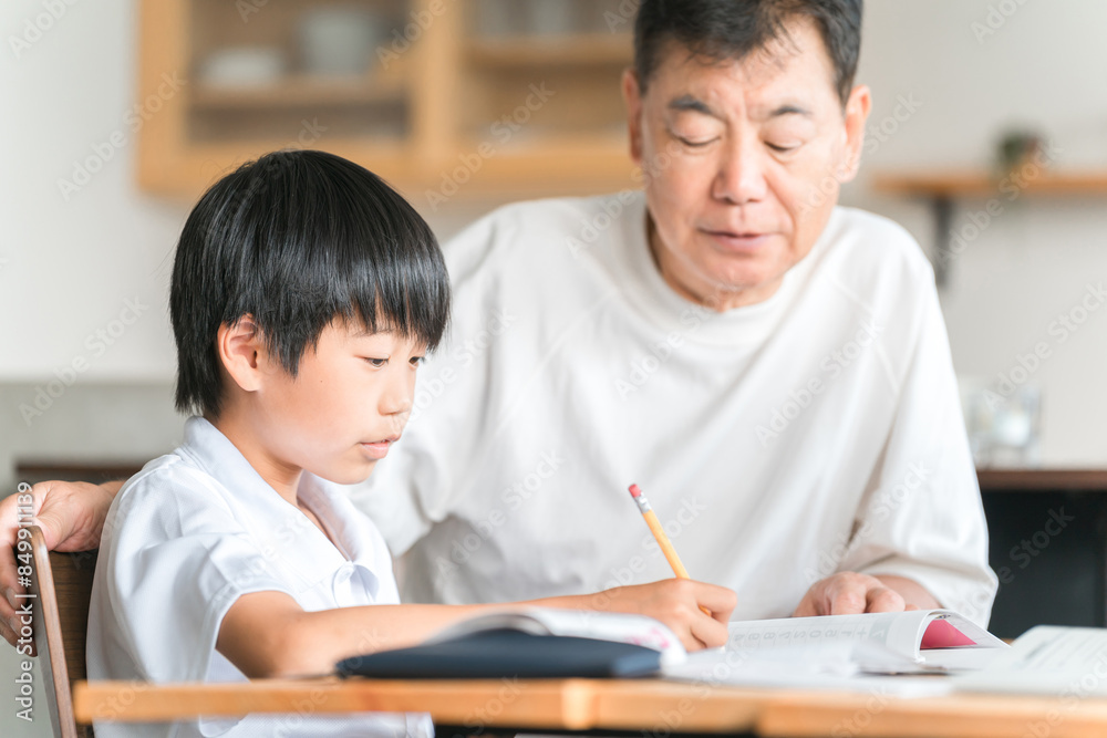 家のダイニングで孫の宿題を教える高齢者男性と小学生の子供
家のダイニングで孫の宿題を教える高齢者男性と小学生の子供