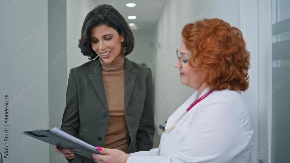 Woman doctor showing papers to visitor in healthcare clinic corridor closeup. Woman doctor showing papers to visitor in healthcare clinic corridor closeup.