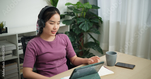 High angle view, Young asian businesswoman wear wireless headphones having a video conference on digital tablet at home office, online meeting for remote work