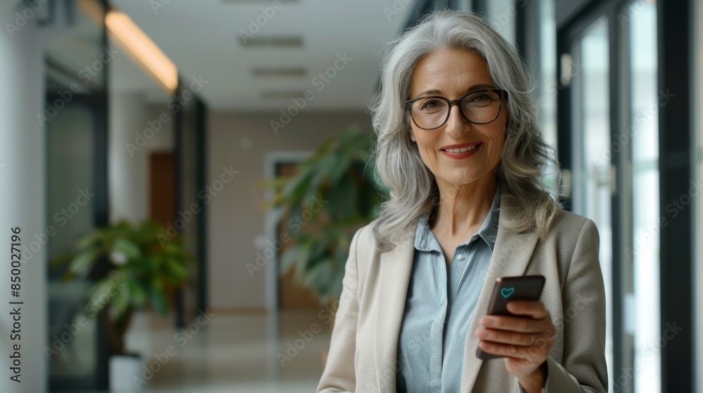 © Photolife - portrait of a confident middle-aged Caucasian business woman in a business suit with a phone looking at the camera while in the office © Photolife - portrait of a confident middle-aged Caucasian business woman in a business suit with a phone looking at the camera while in the office