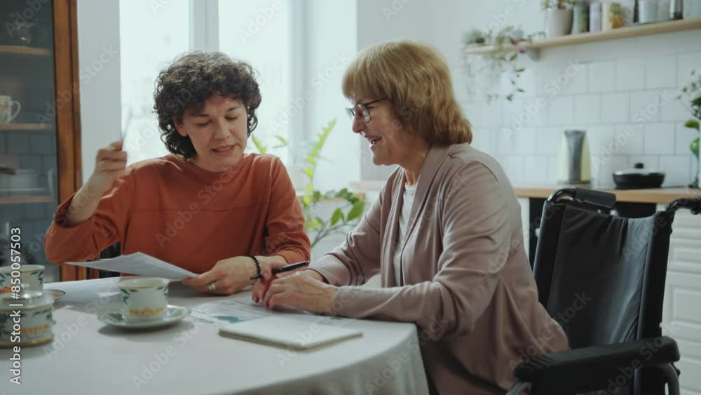Young woman or financial advisor looking through papers and helping senior grandmother with calculating bills at home Young woman or financial advisor looking through papers and helping senior grandmother with calculating bills at home