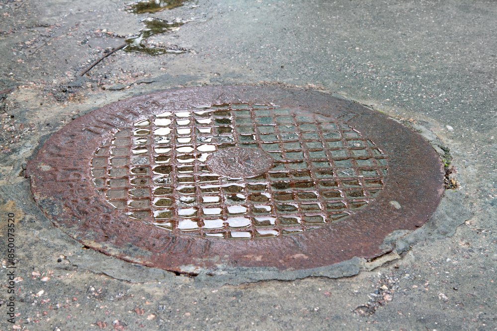 Wet sewer manhole in the asphalt. An old iron sewer manhole. Wet sewer manhole in the asphalt. An old iron sewer manhole.