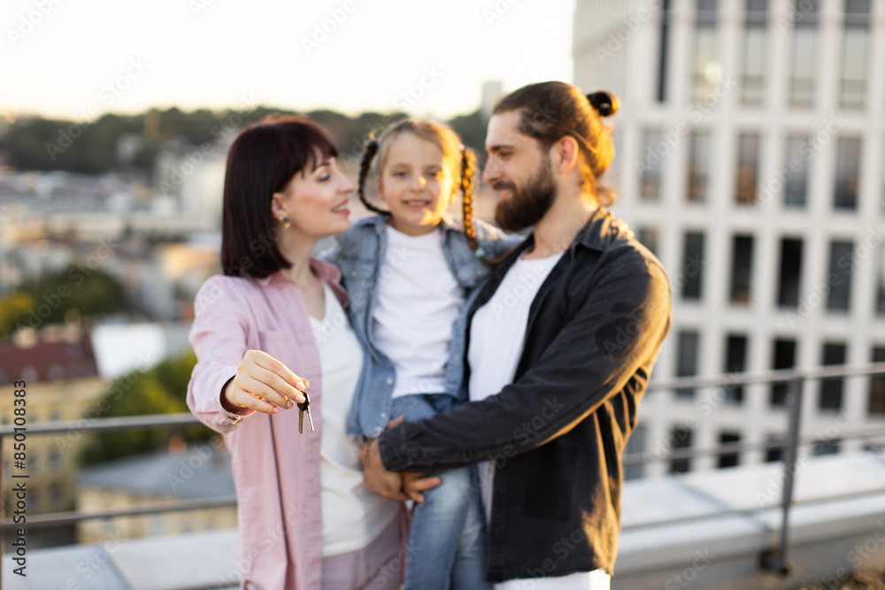 Obraz premium Happy family standing on rooftop, holding keys and celebrating new home with young daughter, representing excitement and togetherness.