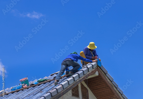 Workers Repairman repairing leaking ridges tile roofing and replace cracked broken tile roofing on  blue  sky  background.