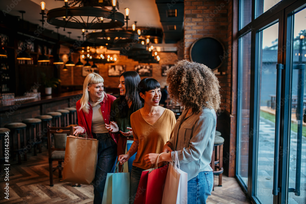 A group of diverse female friends walking into a restaurant, chatting happily with shopping bags in hand A group of diverse female friends walking into a restaurant, chatting happily with shopping bags in hand