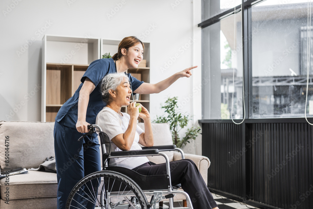 A young female nurse of Asian descent assists an elderly woman in a wheelchair, sitting on a sofa. A young female nurse of Asian descent assists an elderly woman in a wheelchair, sitting on a sofa.