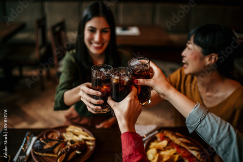 Fotografi Multi-ethnic group of friends sitting in restaurant and cheering with soft drink