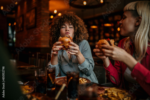 Принти на полотні Hungry woman eating a burger while gathering with friends in a pub
