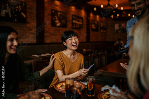 Mid-aged woman paying contactless using a credit card in the restaurant with friends. A group of young people sitting in indoor cafe, paying the bill photo