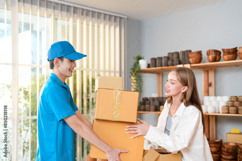 Friendly delivery worker in blue uniform handing several packages to a smiling customer inside a well organized craftwork store for e-commerce Friendly delivery worker in blue uniform handing several packages to a smiling customer inside a well organized craftwork store for e-commerce