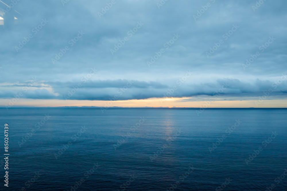 Obraz premium 重い曇天だが、水平線の隙間からかすかに朝日が見えている。 日本国静岡県伊豆半島、伊豆急行線車内 - 2022年10月8日。伊豆半島の海岸線を走る列車、伊豆急行線の車窓からの風景。 