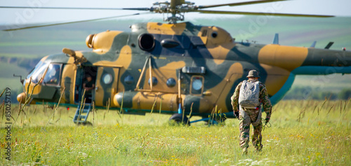 A soldier in camouflage goes to a military helicopter. Military helicopter with soldiers. Armed conflict, hostilities. Air armament, parachutist.