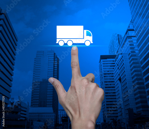 Hand pressing truck flat icon over modern city tower and skyscraper, Truck transportation service concept