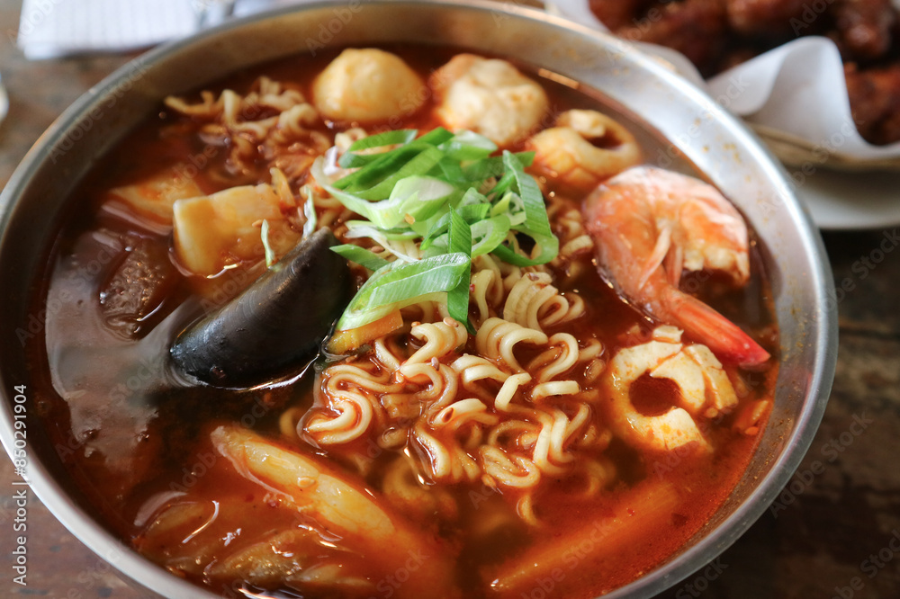 a bowl of noodles or ramyeon with a mixture of green mussels, shrimp, fish balls, meatballs with red tom yum-like. sauce. Korean noodles. Ramen street food. a bowl of noodles or ramyeon with a mixture of green mussels, shrimp, fish balls, meatballs with red tom yum-like. sauce. Korean noodles. Ramen street food.