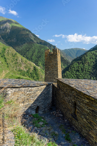 A courtyard with a street, stone buildings, a high tower and a view of the mountains with a gorge. photo