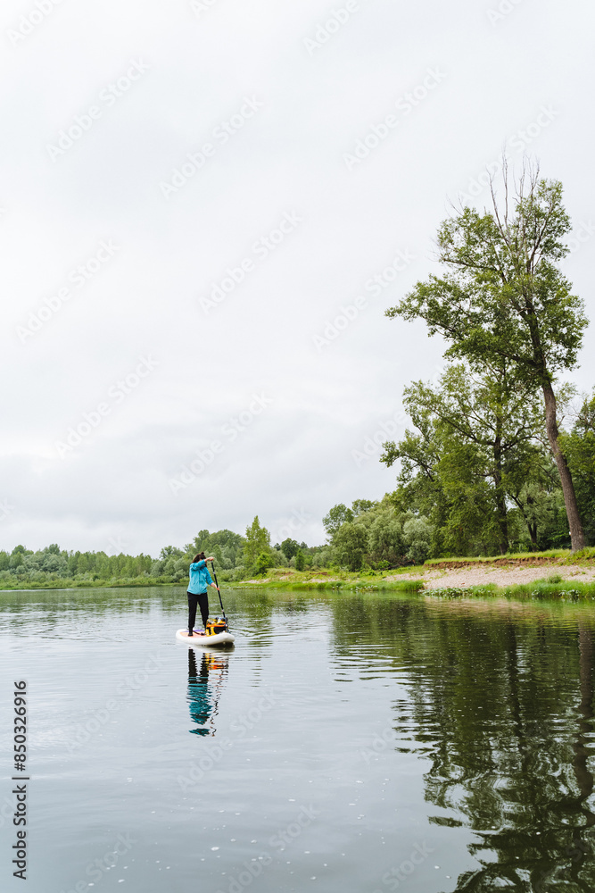 A man is peacefully standing on a paddle board at the center of a serene lake, surrounded by the beauty of nature with clear skies and gentle waters, trees adding to the tranquil scene A man is peacefully standing on a paddle board at the center of a serene lake, surrounded by the beauty of nature with clear skies and gentle waters, trees adding to the tranquil scene